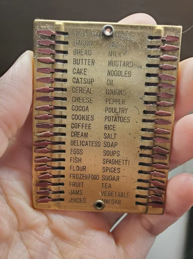 An old metal grocery list with various food items listed, including items like bacon, bread, butter, cake, cereal, cheese, eggs, and more, laid out in a grid format. The item is being held in a hand.
